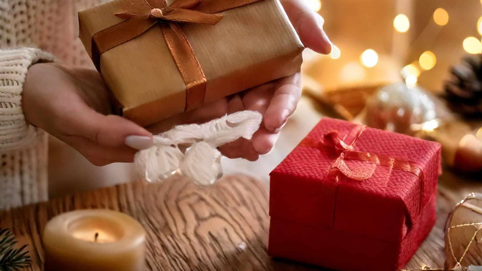 A person holds a gift wrapped in brown paper with a red ribbon above a wooden table, while another hot item in red wrapping lies nearby. The softly lit background with twinkling lights creates a warm, festive atmosphere, reminding you these treasures are going fast this season.